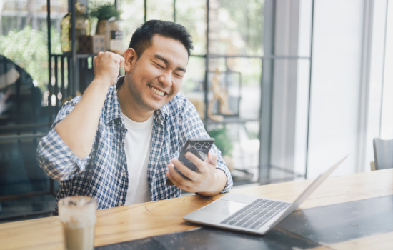 Asian young man in blue shirt working with laptop computer and mobile phone with online job or shopping online happy and smile face in coffee shop cafe